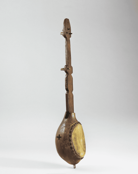 A stringless Haitian banjo with a wooden neck that pierces a rounded gourd body covered with animal 