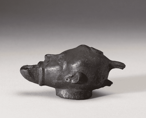 A blackened bronze oil lamp in the shape of a man's head, the open mouth is where the flame would co