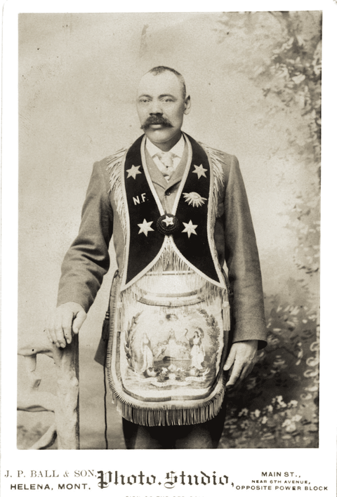 Black and white portrait of a mustachioed man wearing fraternal organization regalia in front of a n