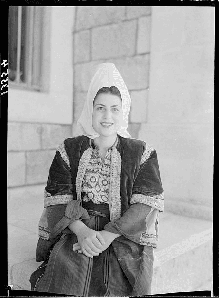 A woman from Bethlehem wearing traditional clothing with embroidery sits for a portrait.