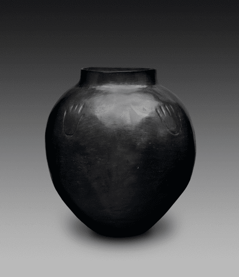 A black ceramic storage jar with a narrow base and lid and a wide body. Two symmetrical bear claw pr