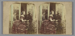 Man en vrouw op een balkon en een tweede vrouw achter glas