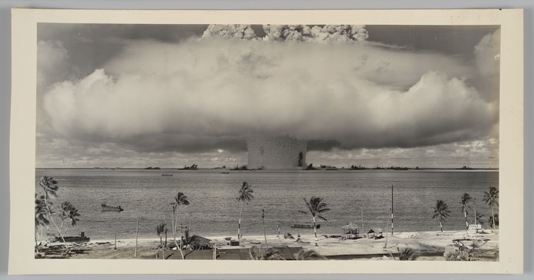 A landscape-oriented, black and white photograph of a nuclear bomb being detonated in the South Paci